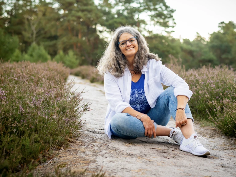 Christina sitzt entspannt auf einem Stein in der Natur.